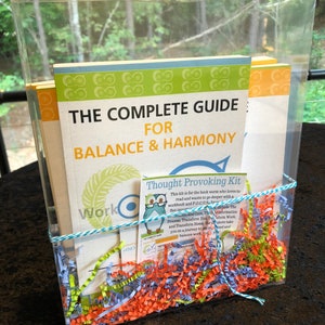 May include: A clear plastic box filled with colorful shredded paper and a book titled "The Complete Guide for Balance & Harmony". A smaller card with the title "Thought Provoking Kit" is visible. The kit includes a workbook and a guide to help readers focus and transform their lives.