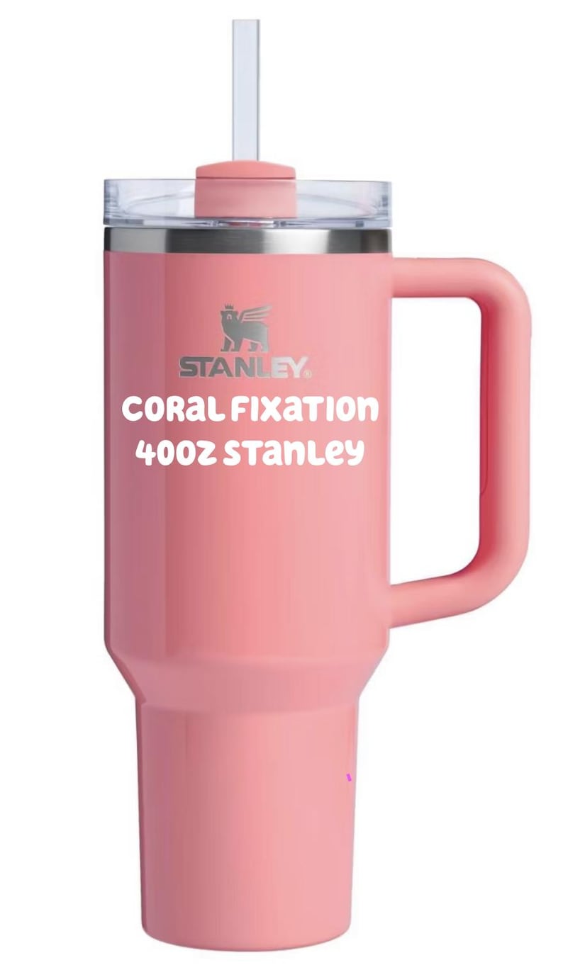 Puede incluir: Un vaso Stanley de color coral de 40oz con asa, tapa transparente y pajita. La taza presenta el logotipo de Stanley y el texto 'CORAL FIXATION 40oz STANLEY' impreso en blanco en la parte frontal. El dise&ntilde;o incluye una base c&oacute;nica y un asa lateral.