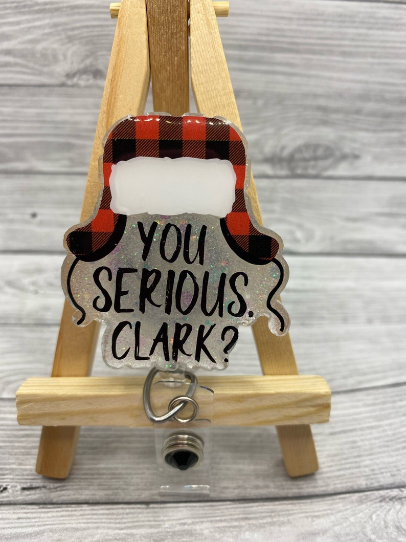 May include: A clear plastic badge holder with a red and black plaid Christmas hat design and the text "You serious, Clark?"  The badge holder has a black retractable reel.