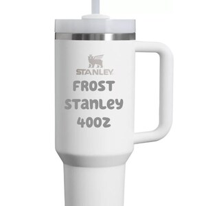Puede incluir: Un vaso t&eacute;rmico blanco con asa, tapa transparente y pajita. El logotipo de Stanley est&aacute; impreso en la parte superior, seguido del texto FROST, STANLEY y 40oz. La taza presenta una base c&oacute;nica y un cuerpo cil&iacute;ndrico con acabado blanco mate.