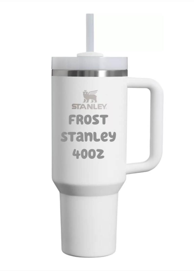 Puede incluir: Un vaso t&eacute;rmico blanco con asa, tapa transparente y pajita. El logotipo de Stanley est&aacute; impreso en la parte superior, seguido del texto FROST, STANLEY y 40oz. La taza presenta una base c&oacute;nica y un cuerpo cil&iacute;ndrico con acabado blanco mate.