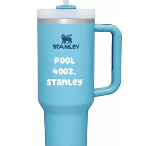 Puede incluir: Un vaso t&eacute;rmico de color azul claro con asa, pajita blanca y tapa. La parte frontal muestra el logotipo de Stanley, el texto POOL, 40oz., y Stanley en letras blancas. El vaso tiene una base c&oacute;nica y un asa vertical en el lado derecho.