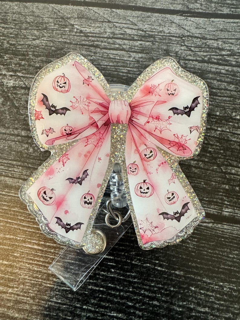May include: A pink glitter Halloween-themed retractable badge holder with a bow and a design of bats and pumpkins.