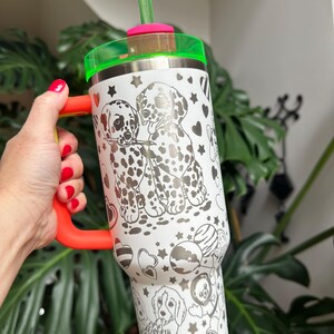 Puede incluir: Un vaso de acero inoxidable blanco con un patr&oacute;n de l&iacute;neas negras de cachorros d&aacute;lmatas, corazones y estrellas. El vaso incluye un asa de color naranja brillante, una tapa transl&uacute;cida de color verde ne&oacute;n y una pajita verde ne&oacute;n a juego.
