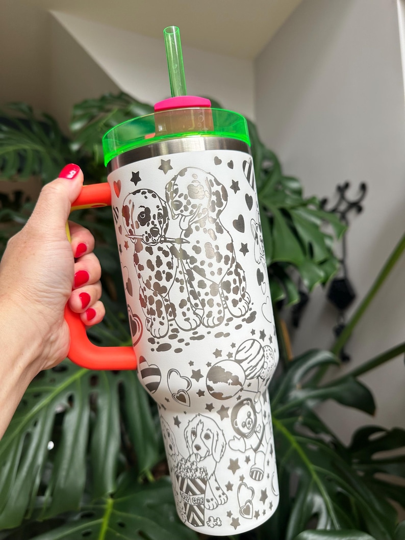 Puede incluir: Un vaso de acero inoxidable blanco con un patr&oacute;n de l&iacute;neas negras de cachorros d&aacute;lmatas, corazones y estrellas. El vaso incluye un asa de color naranja brillante, una tapa transl&uacute;cida de color verde ne&oacute;n y una pajita verde ne&oacute;n a juego.
