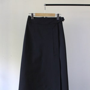 May include: A black wrap skirt with a long, A-line silhouette. The skirt has a single button closure at the waist and a belt loop detail.