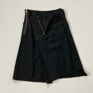 Peut inclure: Jupe asymétrique noire avec une fermeture éclair dorée sur le côté et un bouton à la taille.