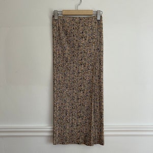 May include: A brown and beige midi skirt with a subtle pattern. The skirt has a slit on the front and is hanging on a wooden hanger.