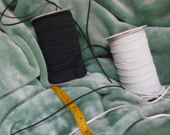 May include: Two spools of elastic cord, one black and one white, are lying on a green fuzzy surface. A yellow measuring tape is also visible.