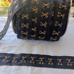 May include: Black fabric trim with gold metal hook and eye closures. The trim is rolled up and tied with a ribbon.