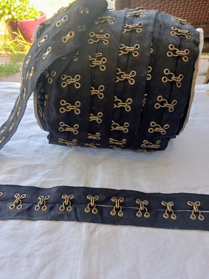 May include: Black fabric trim with gold metal hook and eye closures. The trim is rolled up and tied with a ribbon.