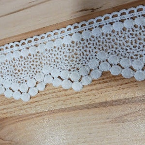 May include: White crochet lace trim with a scalloped edge and small round embellishments.