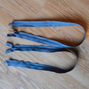 以下が含まれることがあります： 金属製の端が付いた灰色のジッパーの引き手3つ。ジッパーの引き手は木製の表面に置かれています