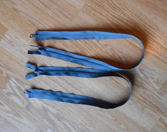 May include: Three grey zipper pulls with metal ends. The zipper pulls are laid out on a wooden surface.