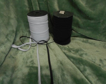 May include: Two spools of elastic cord, one white and one black, on a green fuzzy surface.