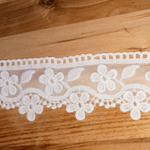 May include: White lace trim with a scalloped edge and floral design. The lace is delicate and intricate, with small flowers and leaves.
