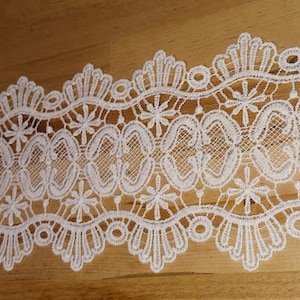 Puede incluir: Borde de encaje blanco con un borde festoneado y un delicado patrón floral. El encaje tiene aproximadamente 2,5 cm de ancho.