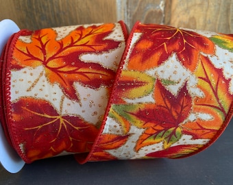 Könnte beinhalten: Eine Rolle weißes Stoffband mit goldener Glitzer-Oberfläche und einem bedruckten Muster aus orangefarbenen, roten und grünen Blättern.
