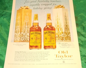 Könnte beinhalten: Zwei Flaschen Old Taylor Kentucky Bourbon Whiskey, eine mit 100 Proof und eine mit 86 Proof, sind in einer festlichen Geschenkverpackung dargestellt. Die Flaschen sind in goldenes Papier mit einem roten Band und Schleife verpackt. Der Text "Old Taylor" ist auf den Flaschen aufgedruckt. Der Text "The Noblest Bourbon of Them All" ist unter den Flaschen aufgedruckt.