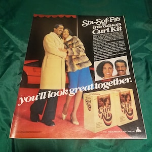 May include: A couple poses together in front of a red car. The woman is wearing a brown fur coat and blue pants. The man is wearing a white coat. The ad text reads "Sta-Sof-Fro introduces Curl Kit you'll look great together." The ad features two boxes of Sta-Sof-Fro Curl Kit hair products.