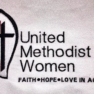 May include: Embroidered logo for United Methodist Women, featuring a stylised flame with a cross inside, and the text "United Methodist Women" in black lettering. Below the logo is the text "FAITH HOPE LOVE IN ACTION".