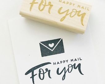 May include: A wooden stamp with the words "For you" and "Happy Mail" in a handwritten style. The stamp is next to a white card with a stamped envelope graphic and the same text.