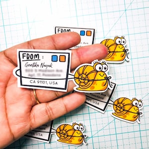 May include: A selection of fun snail stickers and address labels. The stickers show smiling yellow snails with black outlines and a bow. The address labels have the word "FROM" and a name and address.