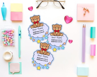May include: Three address labels featuring a cartoon teddy bear on a cloud with stars. Each label has space for a name and address lines. The labels are surrounded by stationery items like pencils, pens, and sticky notes. The text on the labels reads "Your Name, Address Line 1, Address Line 2."
