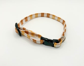 May include: A brown and white checkered dog collar with a black plastic buckle and a silver metal D-ring.