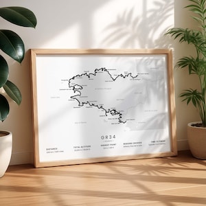 May include: A framed map print of the GR34 hiking trail in France, featuring a black line route on a white background with city names, distance of 2100 km / 1305 miles, total altitude of 20,000 m / 65,616 ft, and highest point of 124 m / 406 ft.