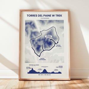 May include: A framed print depicting the Torres del Paine W Trek in Patagonia. The map uses blue and white tones, with the trek route outlined in black. The print includes the text "TORRES DEL PAINE W TREK" and "80 KM / 50 miles".