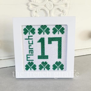 Peut inclure: Broderie au point de croix encadrée en blanc avec des trèfles verts et le texte "March 17"