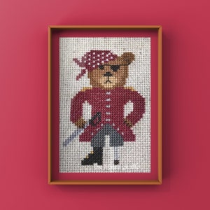 Könnte beinhalten: Kreuzstich-Kunstwerk eines Teddybären-Piraten mit rotem Mantel, Bandana und Augenklappe, der ein Schwert hält. Das gerahmte Stück befindet sich vor einem roten Hintergrund.