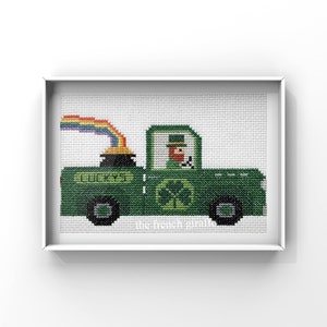 May include: A cross-stitch pattern of a green truck with a pot of gold and a rainbow. The truck has a shamrock on the side and the word "Lucky's" on the back. A leprechaun is driving the truck.