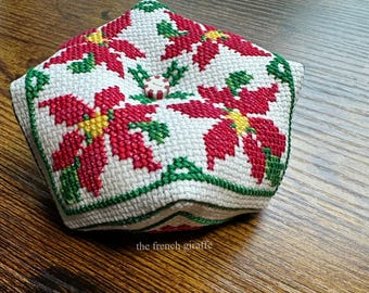Op de afbeelding: Een wit stoffen naaldenkussen met een rood en groen kerststerontwerp. Het naaldenkussen heeft de vorm van een vijfpuntige ster en heeft een knoop in het midden.
