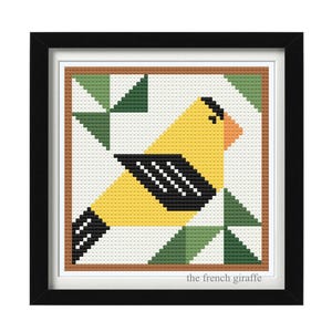May include: Framed cross-stitch art featuring a yellow bird with black and white wings and a brown beak. The bird is set against a white background with green geometric shapes. The frame is black, and the text "the french giraffe" is in the bottom right corner.
