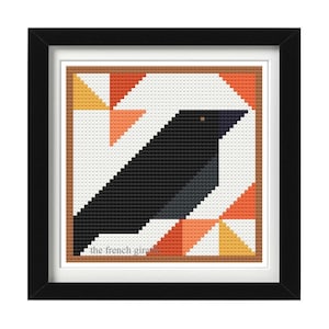 May include: A black crow with a yellow eye is depicted in a framed cross-stitch pattern. The background is a white square with orange and yellow triangles.