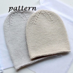 May include: Two knitted beanies in light gray and cream colors. The beanies are made of a soft, textured yarn and feature a ribbed brim. The word "pattern" is written in black cursive at the top.