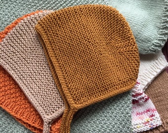 May include: A set of three knitted baby bonnets in different colors: orange, beige, and mustard yellow. The bonnets have ties that can be tied under the chin.