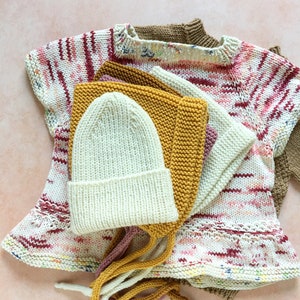May include: A set of three knitted hats in various colors, including cream, mustard yellow, and pink. The hats are made with a textured stitch and have long ties.
