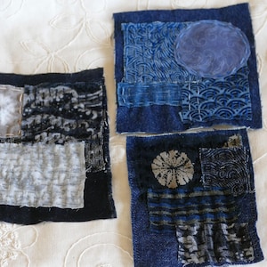 May include: Three small squares of fabric, each made of different blue denim patches sewn together. The patches have various patterns and textures, including a white circle, a wave pattern, and a floral design.