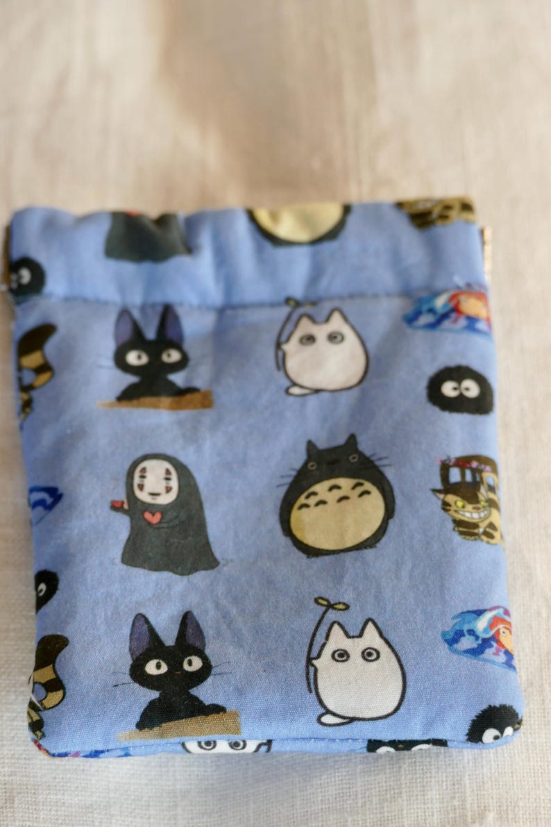 May include: A blue drawstring bag with a variety of cartoon characters from the Studio Ghibli films, including Totoro, No Face, and Jiji the cat.
