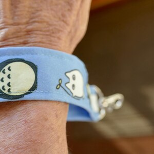 May include: A light blue wristlet with a black and white cartoon character on it. The wristlet has a silver metal clasp.