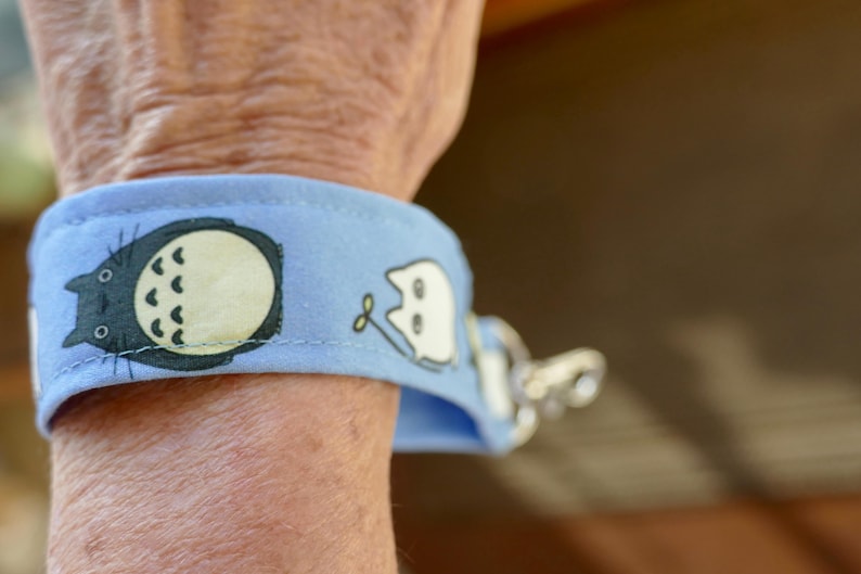 May include: A light blue wristlet with a black and white cartoon character on it. The wristlet has a silver metal clasp.