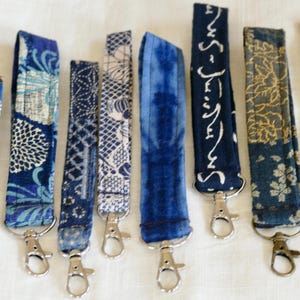 May include: Eight blue and white patterned keychains with silver key rings. The keychains feature different designs, including floral, geometric, and abstract patterns.