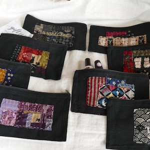 May include: Black zippered pouches with colorful patchwork designs. Some pouches feature cat motifs, while others display geometric and floral patterns. The phrase "Made in Japan" is visible on one pouch.