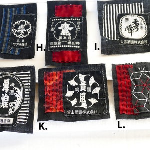 May include: Six black fabric squares with white text and designs. The squares are labeled with letters G, H, I, J, K, and L. The text on the squares includes the words "honni", "Hiroshima", "Sakura", "sake", "today", "store", "island", "rich", "bridge", "mountain", "brewery", "company", "ginjo", "precious", "wind", "富山酒造株式会社", "福本酒造釀", "大合酒造株式会社", "貴風", "吟釀", "清酒", "眞煌", "秀", "酒".