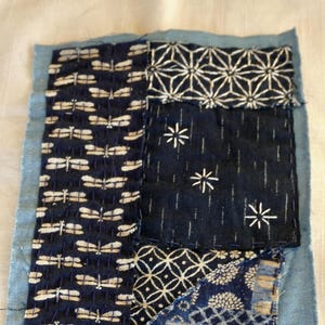 May include: A patchwork of blue and white fabric squares with different patterns, including dragonflies, stars, and geometric designs. The fabric is sewn together with a light blue border.