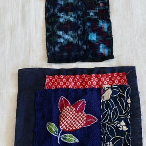 May include: Two rectangular fabric patches featuring layered textile scraps. The top patch displays dark blue and black patterns with red stitching. The bottom patch features a central red and white flower motif on blue fabric with red and floral accents.