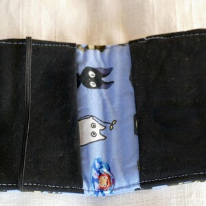 May include: A black fabric wallet with a blue and white fabric lining. The lining has a pattern of cartoon cats and a black cat with white eyes.